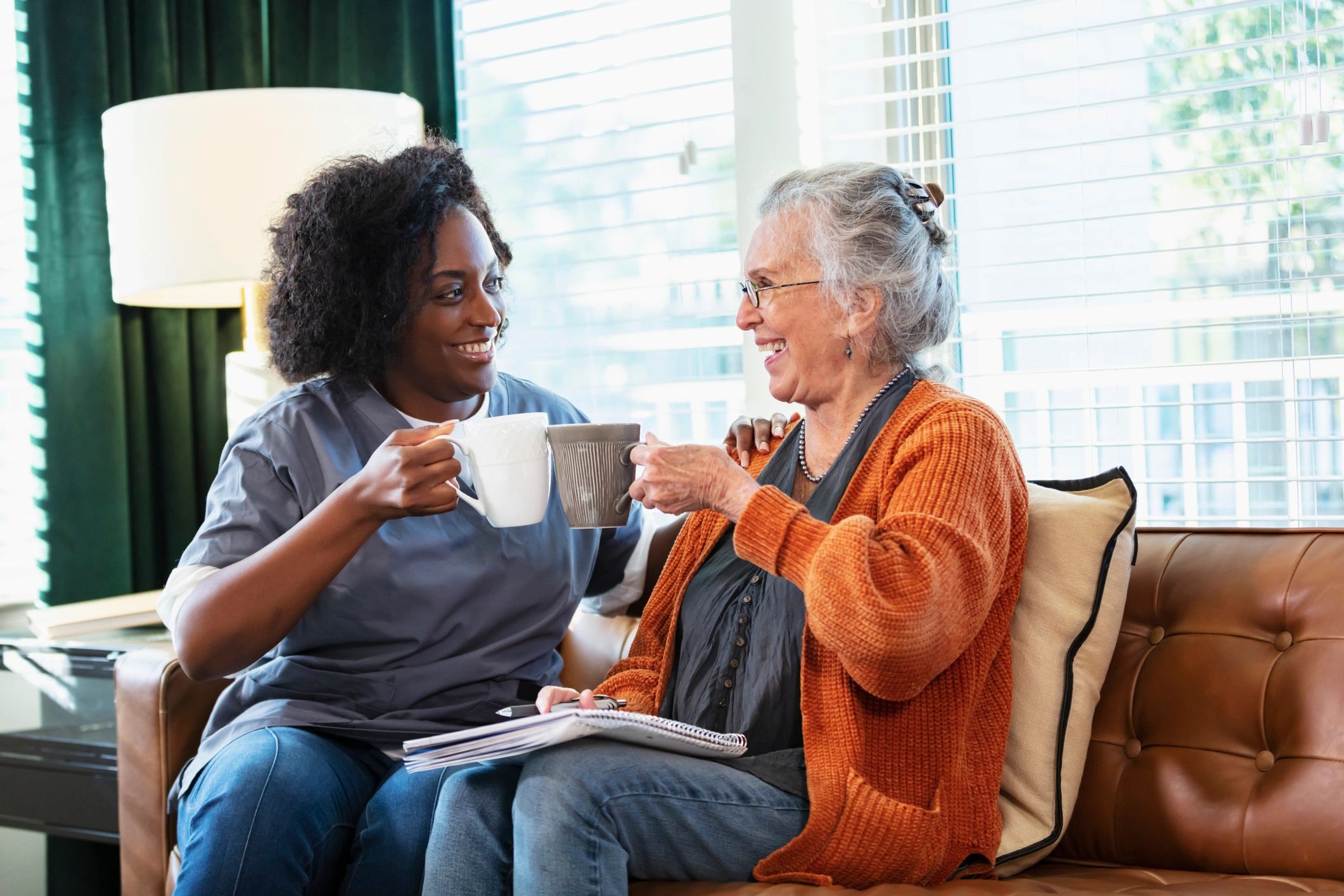 Senior woman having coffee and conversation with a caregiver at home